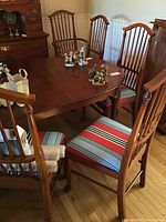 View of dining table edge with three side chairs and two captain chairs in background, showing upholstery stripe pattern and spindle backs.