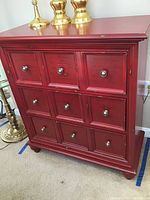 Front view of a red wooden dresser with nine drawer fronts and silver knobs, distressed paint finish.