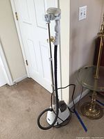 White Home Touch fabric steamer with pole, hose, and handheld steamer attachment shown in room near door and table.