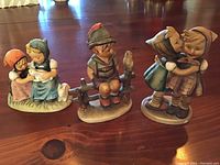 Photo showing all three Hummel figurines arranged side by side on wooden surface