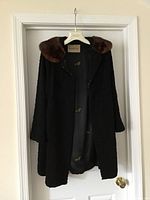 Black lamb coat hanging on a hanger, showing the brown mink collar and interior lining