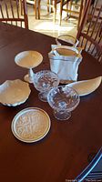 Lenox porcelain pieces including plate, bowls, pedestal dish, and porcelain gift bag along with two clear cut glass candy dishes arranged on a wooden table.
