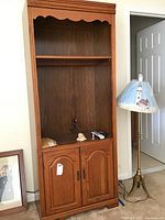 Front view of the wood media cabinet showing upper open shelves and closed bottom cabinet with two doors and metal handles.