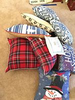 Top view showing nine assorted throw pillows including red plaid, blue floral, blue striped, and holiday themed pillows