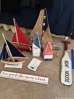 Overview of three wooden sailboats, two wood floats, and two wood signs stacked on carpet