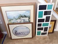 Four framed items grouped: one large blank collage frame with black and teal sections, two rectangular framed prints of countryside scenes, and one smaller horizontally oriented oval art print.