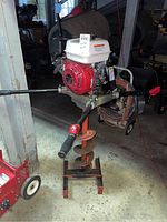 Front view of gas-powered auger upright on metal stand showing engine housing and auger bit
