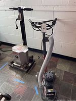 Essex Silver Line floor polisher at left and MK concrete grinder at right on tiled floor against white wall