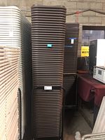 Tall stack of brown folding chairs on black metal cart, adjacent to a stack of white chairs