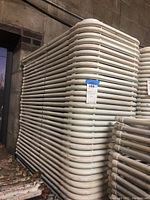 Stacks of white metal folding chairs on a metal cart against a concrete wall.