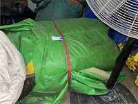 Folded green inflatable bounce house secured with red strap beside a ventilation fan