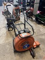 Front perspective view showing orange blower housing, handle and front wheel