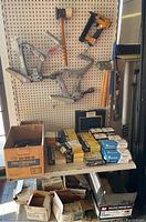 Overall view of pegboard with three manual floor nailers, a Stanley Bostitch pneumatic nailer on the right, mallets at bottom and shelf of nail boxes below