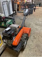 Full front‐three‐quarter view of orange tiller with upright handles and mounted engine