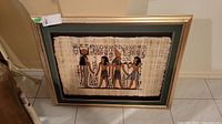 Front view of framed Egyptian art on rice paper showing four Egyptian figures with hieroglyphs and green matte border.