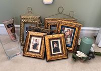 Eight framed prints with gold-tone frames showing classical styled portrait paintings. Also present are a clear glass vase and a green pillar candle with flower decoration.
