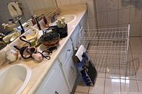 Photo showing ceramic vanity holders, hair styling tools including curlers and blowdryer, wire shelving unit, and other bathroom items on countertop and floor