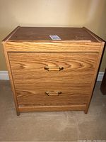 Front view of one bedside table showing two drawers and brass and wood handles.