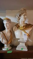 Pair of classical style busts of a man and a woman on wooden surface with price tag on man's bust