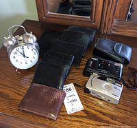Full lot view with both cameras, clock, and eight wallets displayed on a wooden surface in front of a mirror