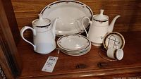 Photo showing the full assortment of Lynns china including platter, two teapots, four small plates, and an espresso cup with saucer arranged in a display case.