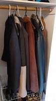 View of five men’s coats hanging in closet, variety of colors and materials including leather and fabric
