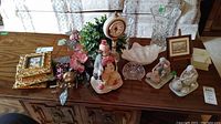 Photo showing collection of items on a wooden sideboard including crystal vase, clown figurines, floral arrangement, framed wall art, clown clock, trinket box, glass candy fish figurines.