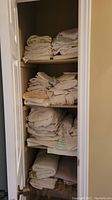 Linen closet shelf with multiple stacks of folded linen including sheets, blankets, and towels