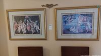 Two wood framed prints hung on a wall above a dark wooden headboard or shelf, showing Botticelli's Primavera on the left and The Birth of Venus on the right.