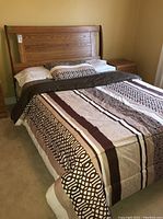 Full view of queen bed made with bedding showing wood frame and comforter with pillow arrangement.