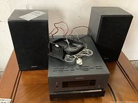 Front view of Sony Micro Hi-Fi receiver between two black Sony speakers with cables on top.