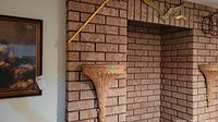 Photo showing two plaster wall sconces mounted on brick wall surrounding fireplace with brass birds and brass garden rake above