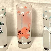 Close-up of frosted cocktail glass featuring orange carousel elephant graphic with carousel pole and canopy design in mid-century style