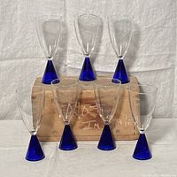 Front arranged view of six cocktail glasses with clear bowls and cobalt blue cone bases on and in front of a wooden block.