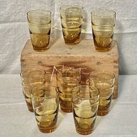 Eight Libbey ripple wave amber juice glasses arranged on and in front of a wooden box. Glasses appear intact without damage.