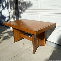 Angled side view of the oak table showing thickness of tabletop and design of panel legs with horizontal support beam.