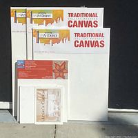 Five artist canvases of various sizes, mostly new in packaging. Three Art District Traditional Gallery Wrapped Canvases in packaging, two smaller standard canvases, white surfaces.