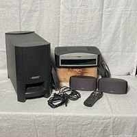 Full setup with subwoofer, main control unit, two satellite speakers, cords, and remote control arranged in front of a white backdrop.