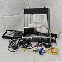 Full view of tattoo kit laid out including machines, needles, power supply, cords, foot pedal, needles in packaging, some inks, and case.