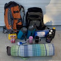 Full view of the camping equipment including backpacks, sleeping bags, bedroll, mugs, brush, and bottles.