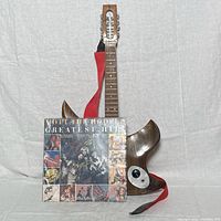 Front view of custom hardwood electric guitar with attached red strap alongside Mott The Hoople Greatest Hits record album cover showing detailed condition and scale.