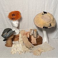 Full display of vintage hats, gloves, camisole, and slippers arranged on hat stands and wooden blocks against a white backdrop.