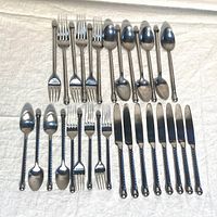 Full assortment shown including forks, spoons, and knives laid out on white cloth background.