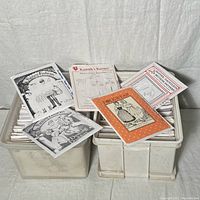 Two white bins filled with many costume sewing patterns in envelopes and packets, some loosely arranged on top showing themes such as fantasy fashion and folkwear.