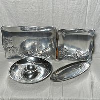 Four pieces of Lenox Butterfly Meadow silver-tone serving ware arranged on cloth background, showing butterfly and floral embossed details on metal surfaces.