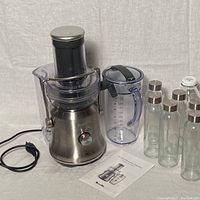 Full view of the Breville juicer unit with the juice pitcher, glass bottles, and instruction manual laid out next to it.