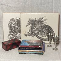Two black-and-white dragon prints by M. Pena, two pewter goblets, a red and black lacquered box, and a stack of fantasy books.