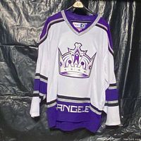Front view of white Los Angeles Kings CCM hockey jersey with purple and silver trimming, large team crown logo and 'ANGELES' text on bottom.