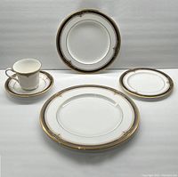 Photo showing one full 5-piece place setting with a dinner plate, salad plate, bread plate, cup and saucer with gilt and black rim decoration.