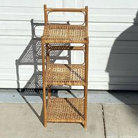 Front view of rattan plant stand showing three woven shelves and stature in natural light.